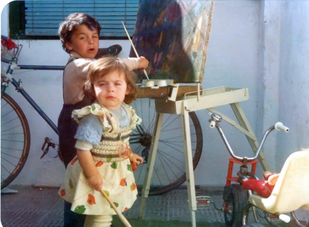 Old photo of Juan Anelo painting as a child in the patio of his family home, next to his sister.